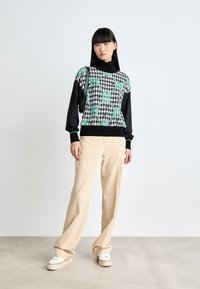 Mustat ja vihreät houndstooth-kuvioidut neuleet, pitkät hihat, ribbireunukset, yhdistettynä beigeihin leveälahkeisiin housuihin ja valkoisiin alustakorkokenkiin.