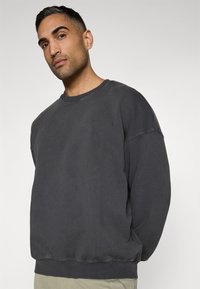 Sweatshirt cinza com um decote redondo, design oversized e punhos canelados. O tecido parece macio, com uma textura ligeiramente usada.