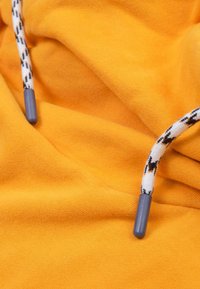 Tissu jaune au toucher doux ; présente un cordon de serrage avec des pointes grises et un cordon à motif blanc avec des accents noirs.