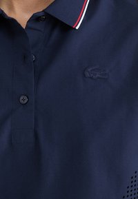 Polo shirt blu navy con maniche corte, apertura con bottoni e colletto a coste con dettagli rossi e bianchi; logo ricamato sul petto.