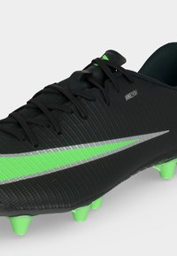 Μαύρο ποδοσφαιρικό παπούτσι Nike με πράσινο και ασημί swoosh, μαύρα κορδόνια και πράσινες τάπες σε λευκό φόντο.