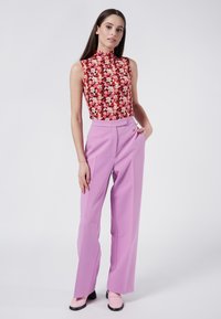 Top sin mangas con estampado floral y un cuello alto, combinado con pantalones anchos lavanda y zapatos rosas, con una textura suave.