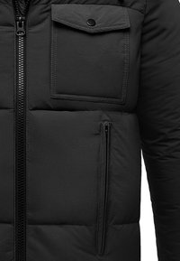 Black puffer jacket featuring quilted texture, two zippered pockets, and a button-flap chest pocket with a sturdy zip closure.