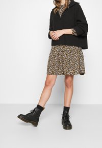 Black ribbed knit sweater layered over a floral print dress. The dress features small white and yellow flowers on a dark brown background. Black lace-up ankle boots with a chunky sole.