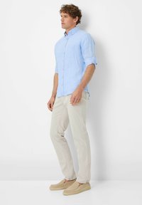Light blue linen shirt with long sleeves and button-up front, paired with light beige pants and tan slip-on shoes.