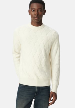 Witte gebreide trui met ruitpatronen, geribbelde ronde halslijn en boorden. Gecombineerd met donkerblauwe jeans. De stof lijkt zacht en gestructureerd.