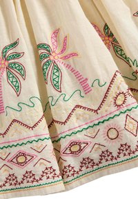Bestickter Stoff mit einem cremefarbenen Hintergrund und vielschichtigen Palmenmotiven in Rosa und Grün, komplizierten geometrischen Mustern am Saum.