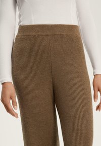 Pantaloni marroni a maglia con un motivo testurizzato, vita alta e cintura elastica, abbinati a un top aderente bianco a maniche lunghe.