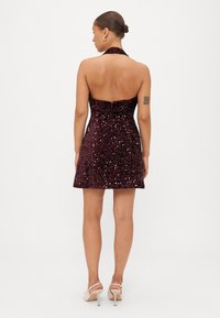 Vestido burdeos de lentejuelas con cuello halter, cuerpo ajustado y falda acampanada, que cuenta con una cremallera en la parte posterior y una textura suave.