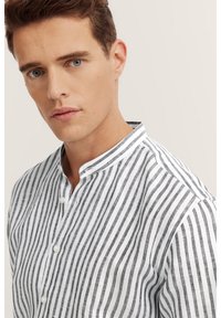 Camicia a righe bianche e nere con colletto alla mandarino, caratterizzata da linee verticali, tessuto leggero e piccoli bottoni lungo la parte anteriore.