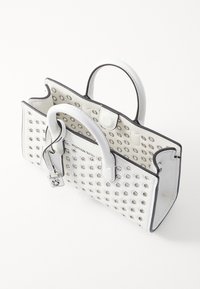 Borsa a mano in pelle bianca con occhielli rotondi in argento, rifiniture nere, doppi manici e un'etichetta pendente con logo. Design esterno testurizzato.