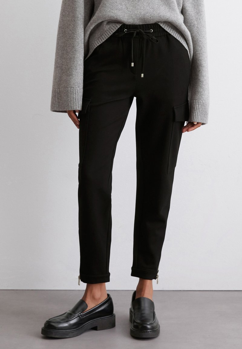 Zwarte cargo broek in een tapered ontwerp met twee zijzakken, een elastische tailleband met trekkoord en ritsen bij de enkels.