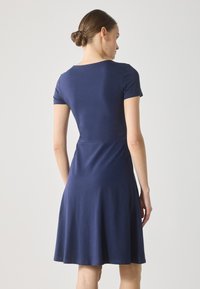 Kortermet marineblå kjole laget av mykt stoff, med en tettsittende liv og utsvevende skjørt. Glatt tekstur med et enkelt, elegant design.