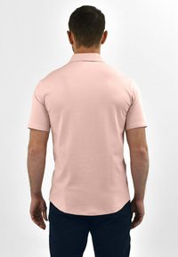 Poloshirt met korte mouwen in zachtroze stof, voorzien van een klassieke kraag en een rechte snit, gecombineerd met donkerblauwe broeken.