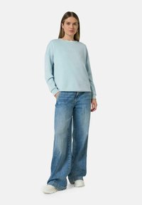 Lichtblauwe sweatshirt met reliëftekst 'CASUAL', gecombineerd met lichtgewassen wijde jeans en witte sneakers. Glad stofgevoel.