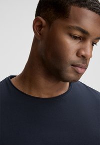 T-shirt blu navy con scollo rotondo e maniche corte, realizzato in un tessuto liscio con dettagli di cucitura sottili.