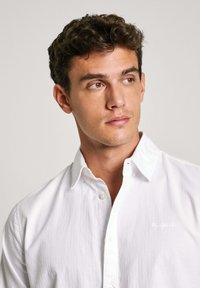 Witte katoenen button-up shirt met kraag, voorzien van een subtiele textuur en een klein geborduurd logo op de borst.