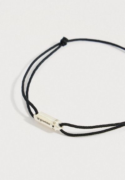 Crna narukvica od kordice s cilindričnom srebrnom kopčom na kojoj je ugravirano "le gramme" i oznaka "925".