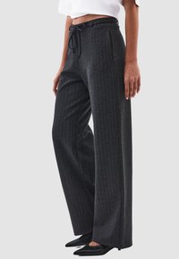 Grijze gestreepte broek met een wijde pijp, een tailleband met trekkoord en voorzakken. De textuur lijkt glad en is gecombineerd met zwarte puntige schoenen.