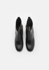 Melnas ādas potītes zābaki ar gludu tekstūru, noapaļotu purngalu un zelta rāvējslēdzēja akcents sānos. Iekšpusē redzams zīmola nosaukums zelta burtiem.