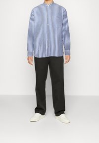 Sinivalkoraidallinen pitkähihaisen nappikauluksen paita, jossa pystykaulus ja rintatasku, yhdistetty mustiin housuihin ja valkoisiin tennareihin.