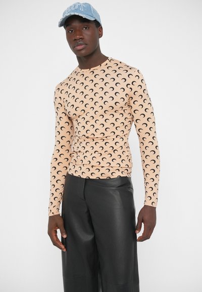 Hosszú ujjú felső halvány barackszínben, fekete félhold mintával, fekete műbőr nadrággal párosítva. Puha, rugalmas anyag, testhez simuló szabás.