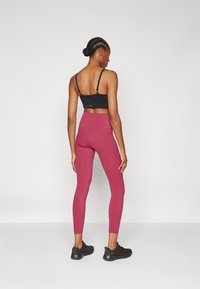 Soutien-gorge de sport noir à fines bretelles, associé à un legging taille haute et ajusté de couleur bordeaux, doté de poches latérales et d'une texture lisse.