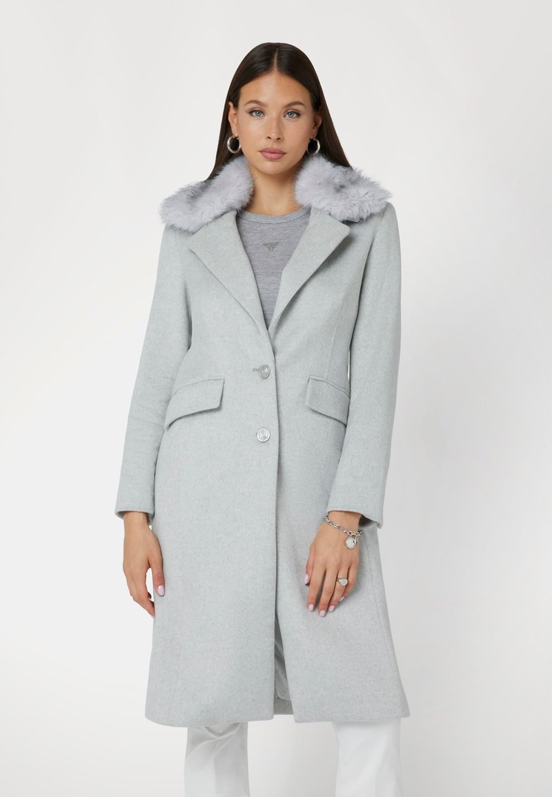 Cappotto in lana grigio chiaro con un morbido colletto in pelliccia sintetica grigia, due tasche frontali e chiusura con un solo bottone. Maniche lunghe e design fino al ginocchio.