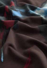 Bruine stof met een zachte textuur, met abstracte patronen in blauw, rood en zwarte tinten, zacht gedrapeerd en gerimpeld.