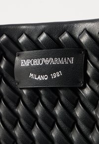 Black leather bag featuring woven texture, a logo tag embossed with "EMPORIO ARMANI" and "MILANO 1981" in silver lettering.