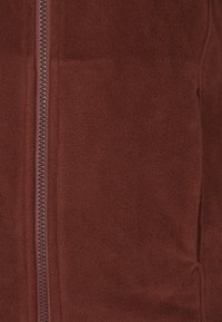 Giacca a zip in pile marrone con una texture liscia, cerniera centrale e tasche laterali. Design semplice senza motivi o accentuazioni visibili.