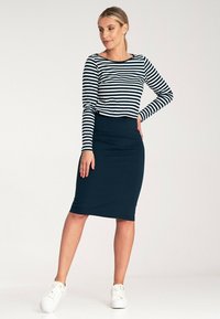 Granatowa bluzka w białe paski z długim rękawem połączona z dopasowaną granatową spódnicą i białymi sneakersami, tworząc zwarty, codzienny zestaw.