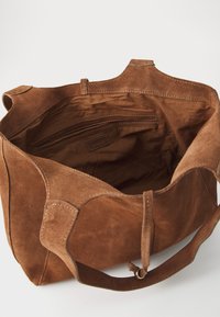 Sac fourre-tout en suede marron avec une texture douce, ouverture sur le dessus et poche zippée à l'intérieur. Doté de poignées renforcées et d'accents cousus. Design spacieux.