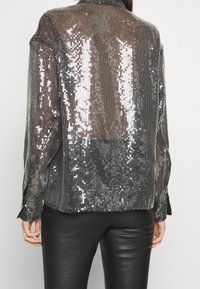 Blusa nera trasparente con paillettes, dotata di colletto, maniche lunghe e una vestibilità ampia, che mette in mostra una texture scintillante e dettagli riflettenti.