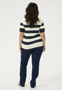 Stripet striktrøje i marineblå og creme, korte ærmer, buet kant. Sammen med mørkeblå jeans og flade sko. Glat tekstur og tætsiddende form.