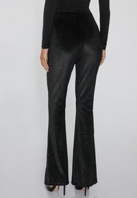 Zwarte wijde broek van gestructureerd materiaal met een diamantpatroon en een glanzende afwerking, voorzien van een getailleerde taille en een uitlopende zoom.