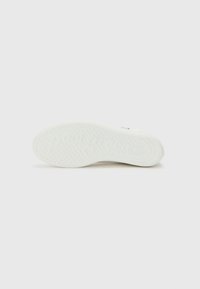 Weiße Sneaker-Sohle mit einer strukturierten Gummi-Oberfläche, die kreisförmige Muster und geprägte Markenkennzeichnung aufweist, flaches Design mit leicht abgerundeten Kanten.