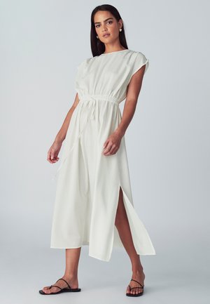 Hvid midi kjole med korte ærmer, elastisk talje, sidesplidser og glat tekstur. Båret med sorte flade sandaler.