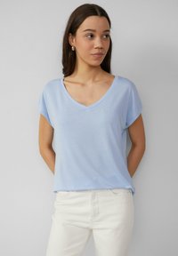 Jasnoniebieska koszulka V-neck z krótkimi rękawami, wykonana z miękkiego materiału. Połączona z białymi dżinsami, prezentującymi luźny krój. Prosty design.