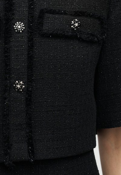 Μαύρο υφασμάτινο σακάκι με υφή, κοντά μανίκια, διακοσμημένο με έξω περιθώρια, τσέπη με καπάκι και διακοσμητικά κουμπιά σε σχήμα κρυστάλλινου λουλουδιού.
