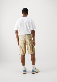 White cotton t-shirt, beige cargo shorts with multiple pockets and a slightly loose fit, paired with neutral-toned athletic shoes and white socks.