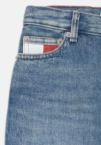 Jeans in denim con una tonalità blu chiaro, design classico a cinque tasche, bottone in metallo e un piccolo tag bianco e rosso visibile nella tasca.