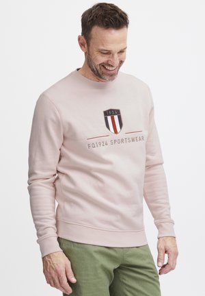 Vaaleanpunainen huppari, joka on valmistettu pehmeästä kankaasta. Edessä on logo, jossa on vuosiluku 1924, sekä teksti "FQ1924 SPORTSWEAR."