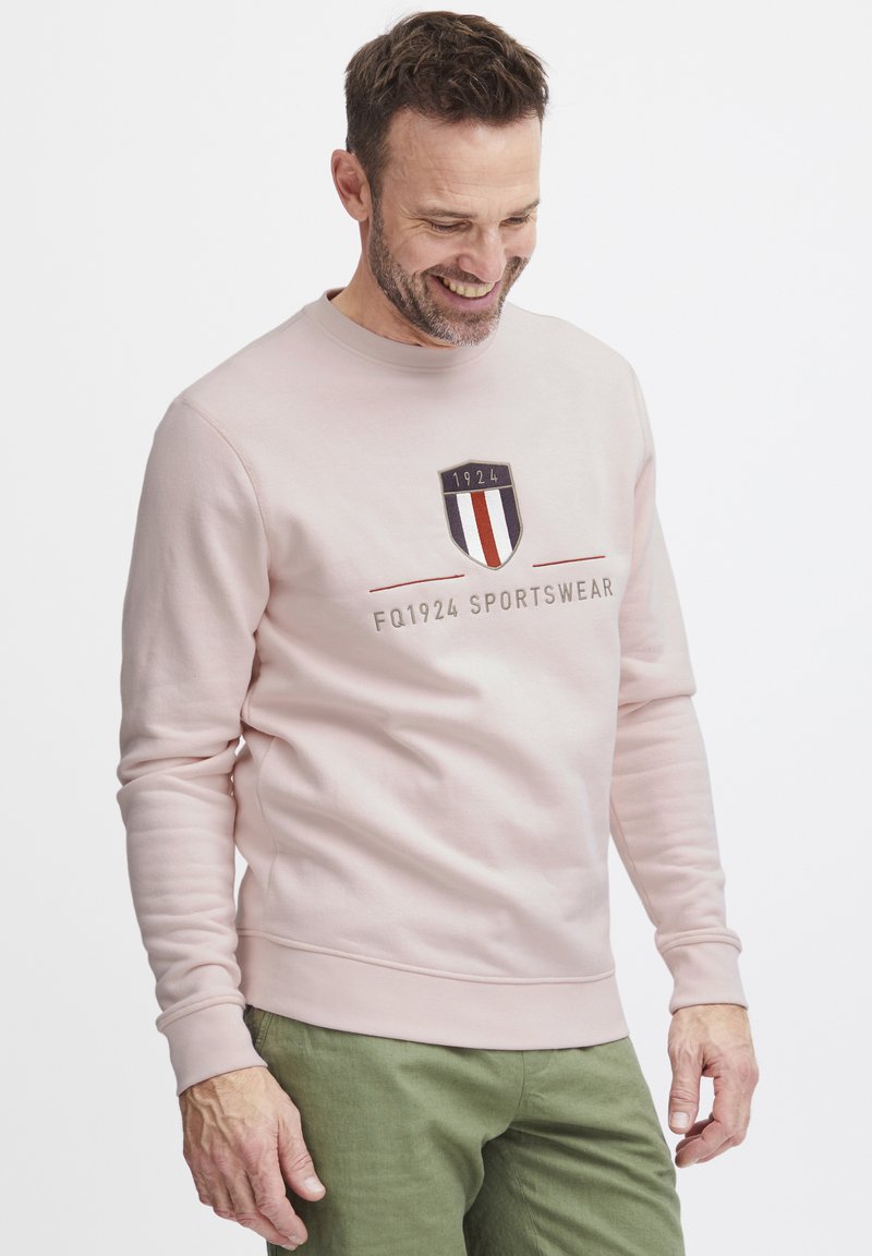 Felpa rosa chiaro in tessuto morbido, con un logo a scudo frontale che presenta l'anno 1924, accompagnato dal testo "FQ1924 SPORTSWEAR."