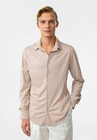 Lichtbeige langslavige shirt gemaakt van zachte stof, met een knoopsluiting aan de voorkant, een puntige kraag en een licht gebogen zoom.