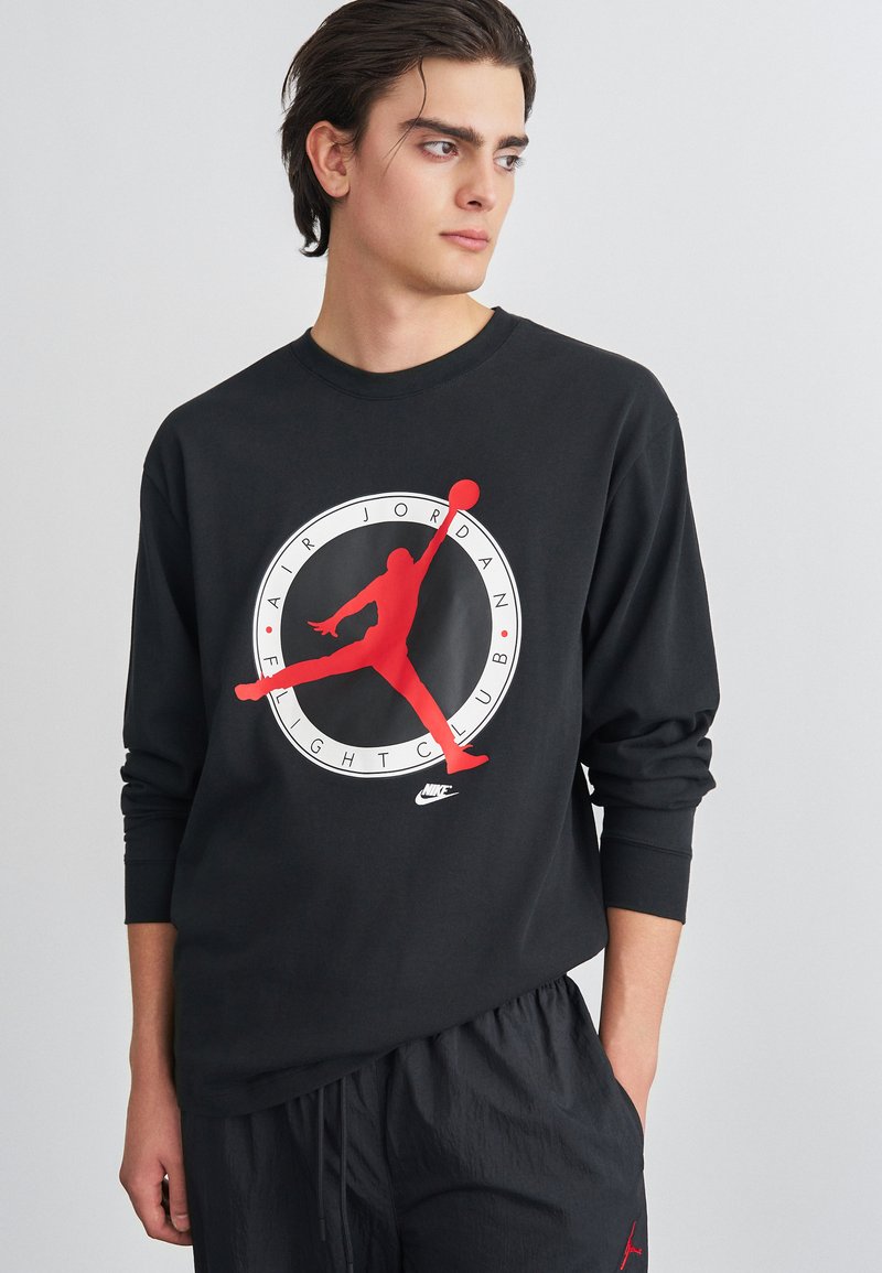 Μαύρη μακρυμάνικη μπλούζα με μεγάλο κόκκινο και λευκό γραφικό ενός άλματος σιλουέτας σε κυκλική σχεδίαση. Μαλακό βαμβακερό ύφασμα.