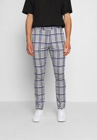 Harmaat ruudulliset housut sinisillä yksityiskohdilla, istuva muotoilu, sileä pinta ja keskipitkä vyötärö, yhdistettynä valkoisiin lenkkareihin. Musta t-paita yllä.