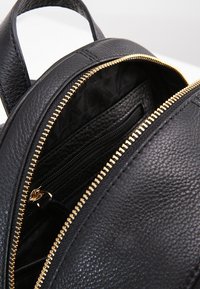 Sac à dos en cuir noir avec une surface texturée, une fermeture éclair dorée et une poche zippée intérieure avec un motif subtil.