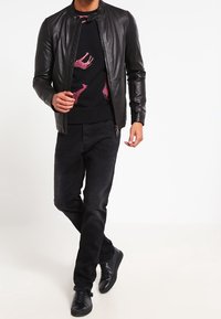 Chaqueta bomber de cuero negro sobre un suéter negro con estampados de animales en rosa, combinada con jeans negros y zapatillas negras.