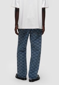 Jeans in denim azzurro chiaro con un motivo logo in tutta la superficie di una tonalità più scura. Vestibilità ampia con tasche standard e dettagli in cucitura scura.